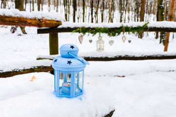 Naklejka premium Blue lantern on snow and hearts hanging with fir garland in the garden