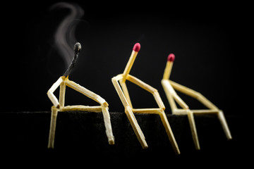 three characters made of matchsticks sad and sitting in the dark, one away from the other. One of...