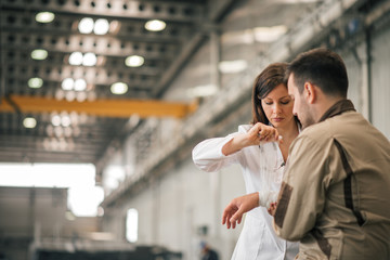 Beautiful female medic bandaging injured worker's hand at industrial factory hall.