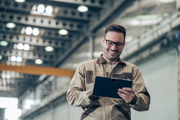 Portrait of a smiling factory engineer, low angle image. Handsome man looking at tablet while...