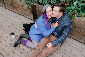 Couple is sitting in an embrace on a wooden floor on the street. Woman and man smile.