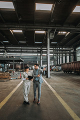 Manager walking and talking with factory employee at metal industry factory.