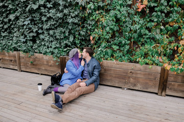 Couple is sitting in an embrace on a wooden floor on the street. Woman and man smile.