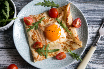 Crepes with eggs, cheese, arugula leaves and tomatoes. Galette complete. Traditional dish galette sarrasin.