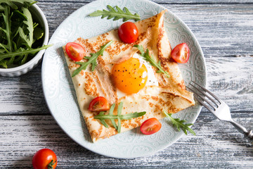 Crepes with eggs, cheese, arugula leaves and tomatoes. Galette complete. Traditional dish galette sarrasin.