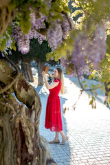 Obraz premium Girl in red dress smiling taking selfie picture in wisteria garden.