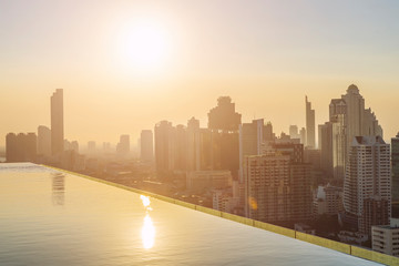 Modern building in Bangkok city with swimming pool in foreground at sunset.