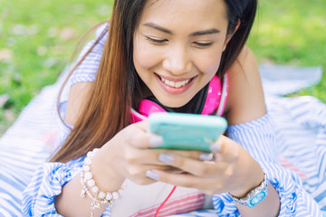 Young woman using smartphone for working, connecting to people and listening music in park. Modern technology for life concept.