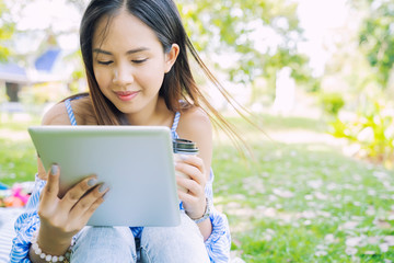 Fototapeta premium Young asian woman in casual using laptop while drinking coffee in garden with happy. Technology for life concept.