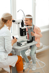 Smiling little girl in pink shirt sitting in front of attentive doctor - obrazy, fototapety, plakaty
