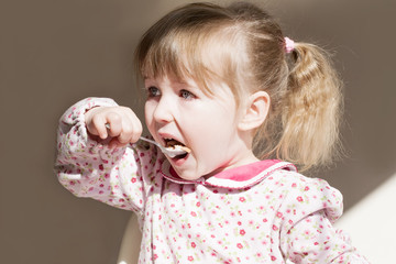 funny white child girl face with spoon in open mouth closeup view