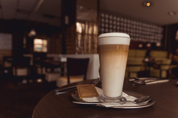 Cup of caffe latte with set of cutlery on brown table in coffeehouse