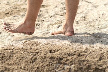 Fototapeta na wymiar Closeup view of bare human feet on sand beach background. Summer vacation concept 