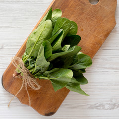Top view, fresh raw spinach on a rustic wooden board on a white wooden surface. Flat lay, overhead,...