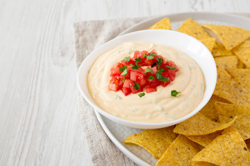 Homemade cheesy dip in a bowl, yellow tortilla chips, side view. Space for text.
