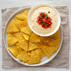 Homemade cheesy dip in a bowl, yellow tortilla chips, top view. Close-up. Flat lay, overhead, from above.