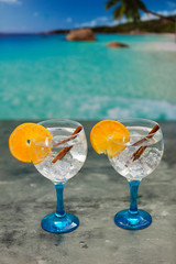 Two gin tonics on blue glass with cinnamon and orange vertical shot