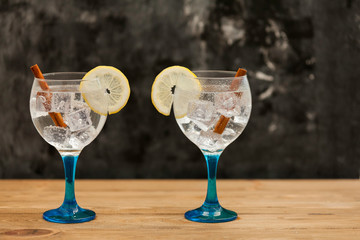 Two gin tonics on blue glass with lemon and cinnamon on wooden table