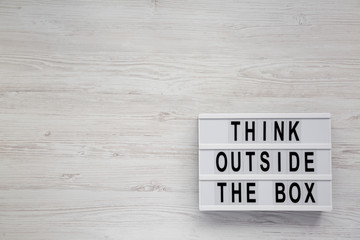 'Think outside the box' words on a modern board on a white wooden surface, top view. Flat lay, overhead, from above. Copy space.