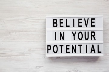 'Believe in your potential' words on a modern board on a white wooden background, top view. Copy space.