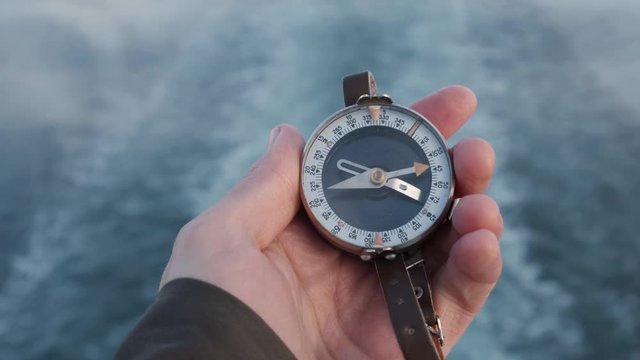 Close up on compass instrument in gloved hand . Mountain hiking trails. background river