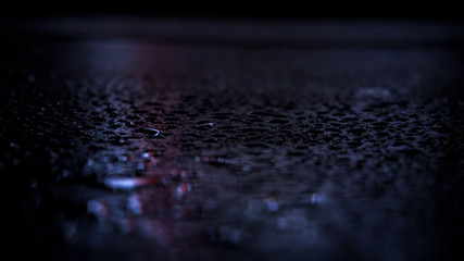 Dark background. Spilled liquid on the mirror surface, the reflection of neon lights, glare, blurred bokeh background. Neon, night view of the streets of a big city.