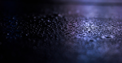 Dark background. Spilled liquid on the mirror surface, the reflection of neon lights, glare, blurred bokeh background. Neon, night view of the streets of a big city.