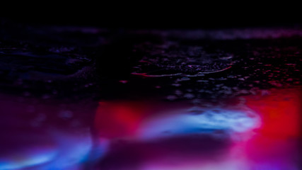 Dark background. Spilled liquid on the mirror surface, the reflection of neon lights, glare, blurred bokeh background. Neon, night view of the streets of a big city.