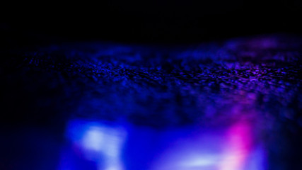 Dark background. Spilled liquid on the mirror surface, the reflection of neon lights, glare, blurred bokeh background. Neon, night view of the streets of a big city.