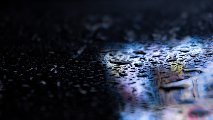 Dark background. Spilled liquid on the mirror surface, the reflection of neon lights, glare, blurred bokeh background. Neon, night view of the streets of a big city.
