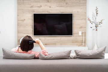Back view of beautiful young woman resting in luxury appartments, sitting on the sofa and watching...