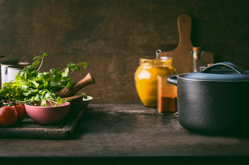Food background with cast iron cooking pot, fresh seasoning and spices on rustic kitchen table....