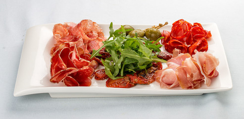 Appetizers of Italian sausages. Prosciutto, chorizo, pancetta and salami. Capers, arugula and sun-dried tomatoes. On white background