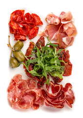 Appetizers of Italian sausages. Prosciutto, chorizo, pancetta and salami. Capers, arugula and sun-dried tomatoes. On white background