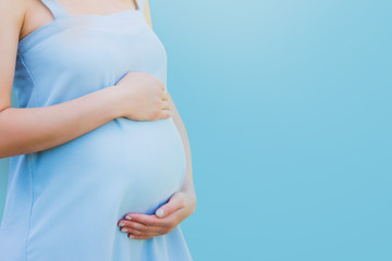 A pregnant woman in a blue dress on a blue background. Pregnancy, parenthood, motherhood concept. Love for children concept with copy space.