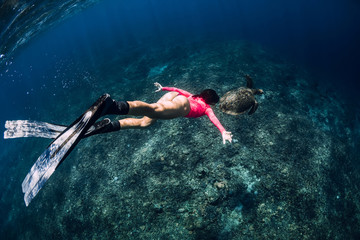 Young woman freediver with fins swim underwater with sea turtle.