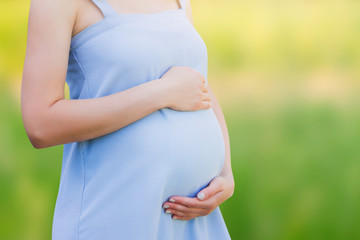 A pregnant woman in a blue dress on a nature background close-up. Pregnancy, parenthood, motherhood concept. Love for children concept with copy space.