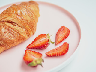 Summer breakfast. Pink plate with croissants and strawberry. Close Up
