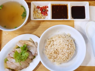 Top view of Steamed chicken with rice, clear soup and bean sauce on wooden table as a background, Hainanese chicken rice set, Khao Man Kai  is Thai traditional, Ready to eat or serve