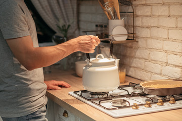 Late night tea habit. Cropped shot of man putting old style kettle on stove. Modern kitchen background.