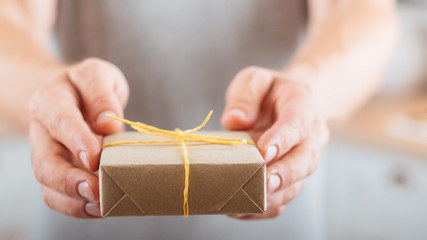 Birthday gift. Cropped shot of man giving present wrapped in rustic style paper. Blur background.
