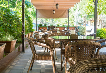 tables and wicker chairs in outdoor summer cafe with flower beds