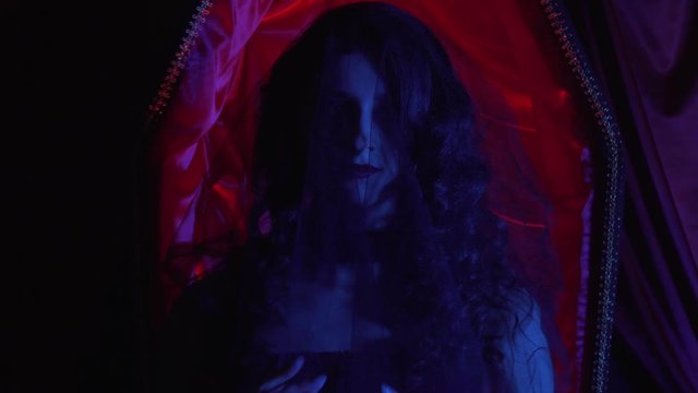 Young woman with black veil on her head and a coffin on the background, 4k