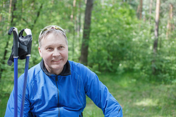 Naklejka na ściany i meble Adult man in blue jacket pose Nordic walking in the Park
