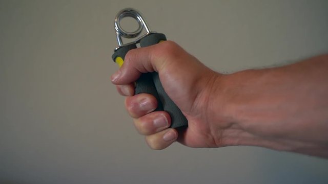 Slow motion of a man working on his grip and forearm strength with a handgrip strengthener (120fps to 30 fps)