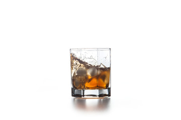 Whiskey splash from the fallen ice cube into glass with beverage on light background..