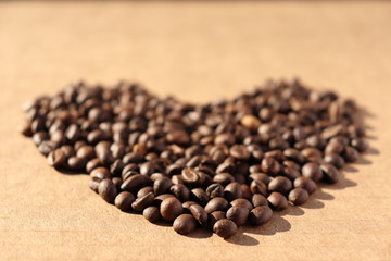 Spilled coffee. Grains of aromatic roasted coffee scattered in the form of a heart on a cardboard surface in the rays of the rising sun.