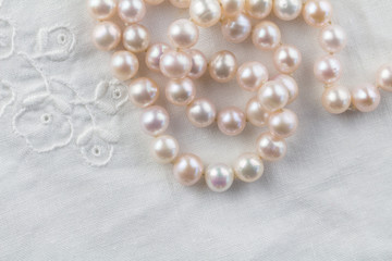 Pearl necklace on white embroidered linen background - top view of string of pink pearls