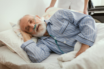 Sick elderly man wearing blue pajama lying in bed at nursing home