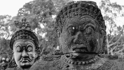 Two ruined angry face statues on the road outside the ancient city of the Khmer empire - Angkor Thom. (Angkor Wat, Siem Reap, Cambodia)